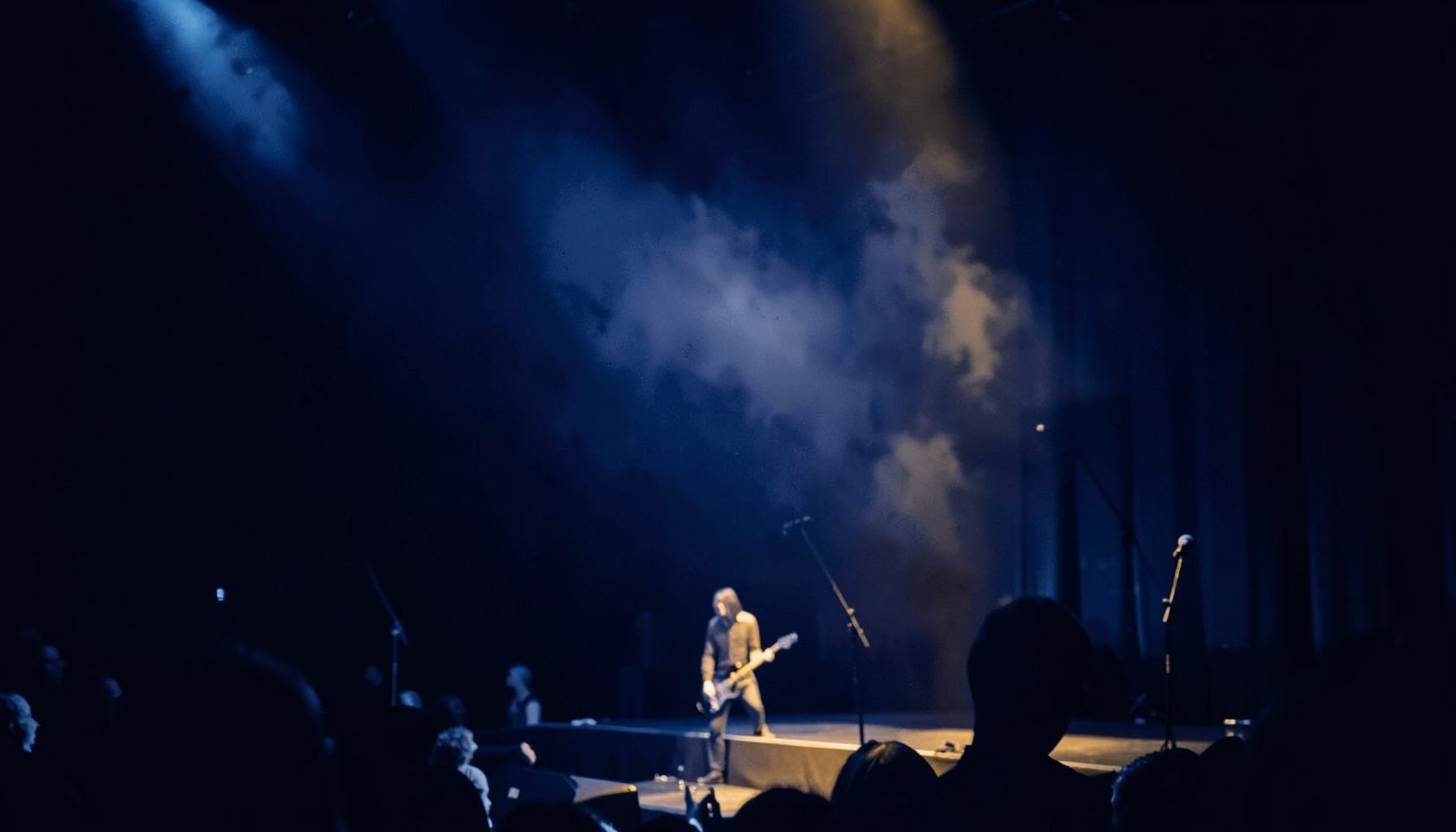 A duotone photograph in indigo and warm amber showing a stage with dramatic lighting and a microphone stand, evoking the atmosphere of a live sports broadcast