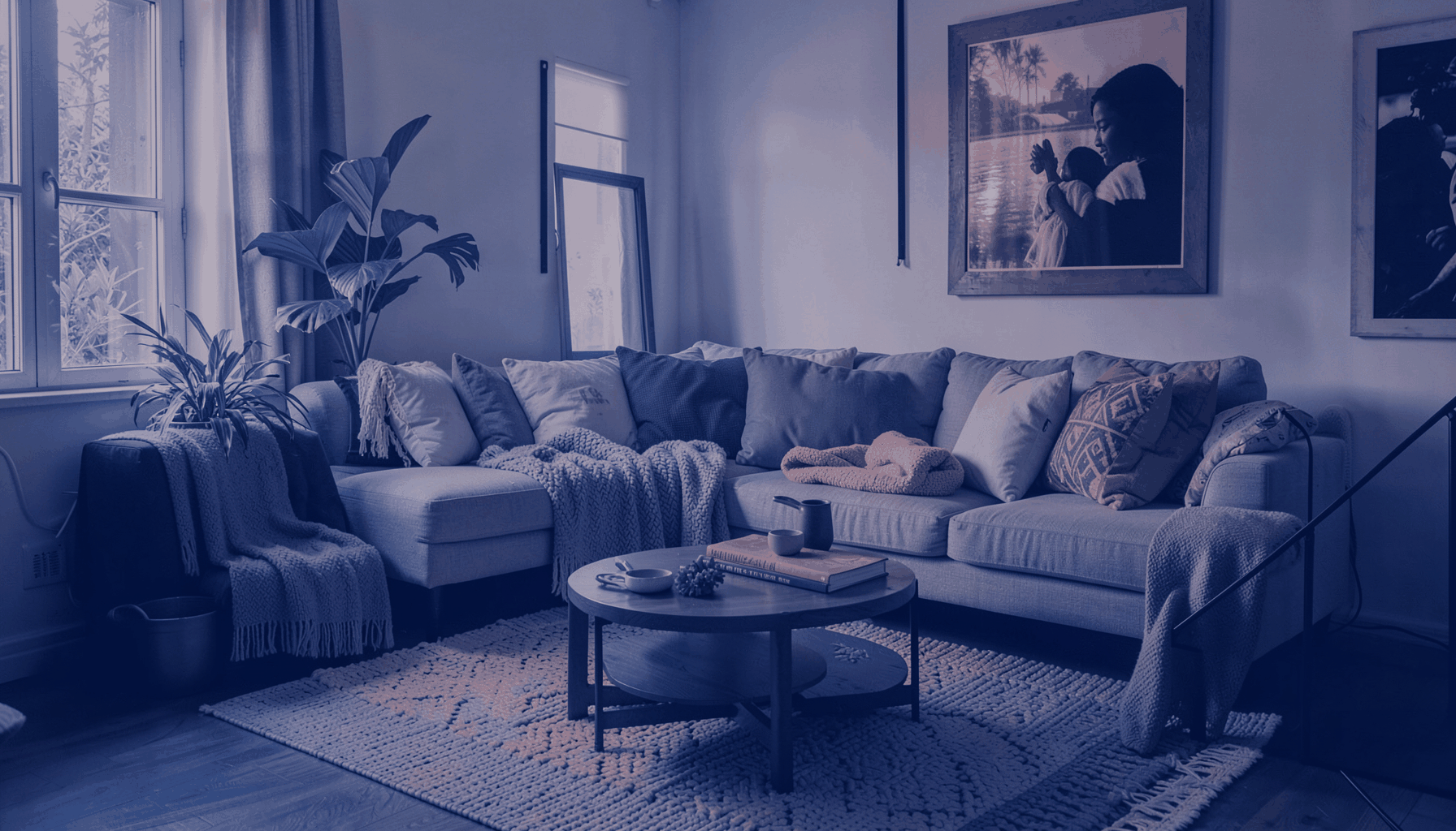 A duotone photograph in deep indigo and warm coral pink showing a thoughtfully arranged living space with textiles and soft furnishings, conveying elegance and personal style.